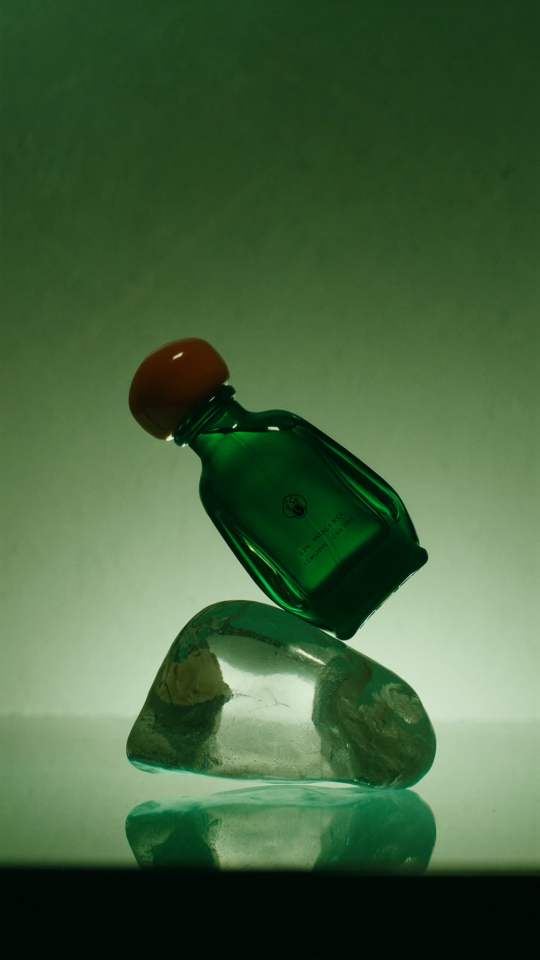Product shot of a green glass fragrance bottle balanced on a crystal