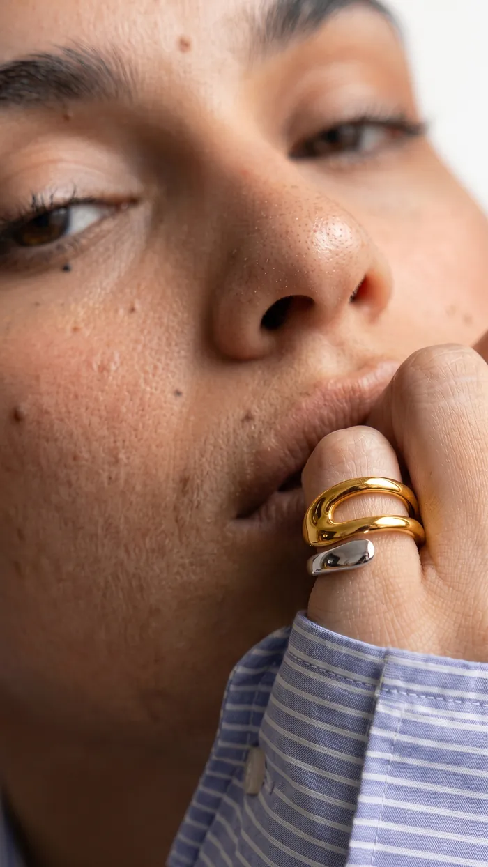 Close-up of stacked F&eacute;bae gold rings in a UGC-style product ad